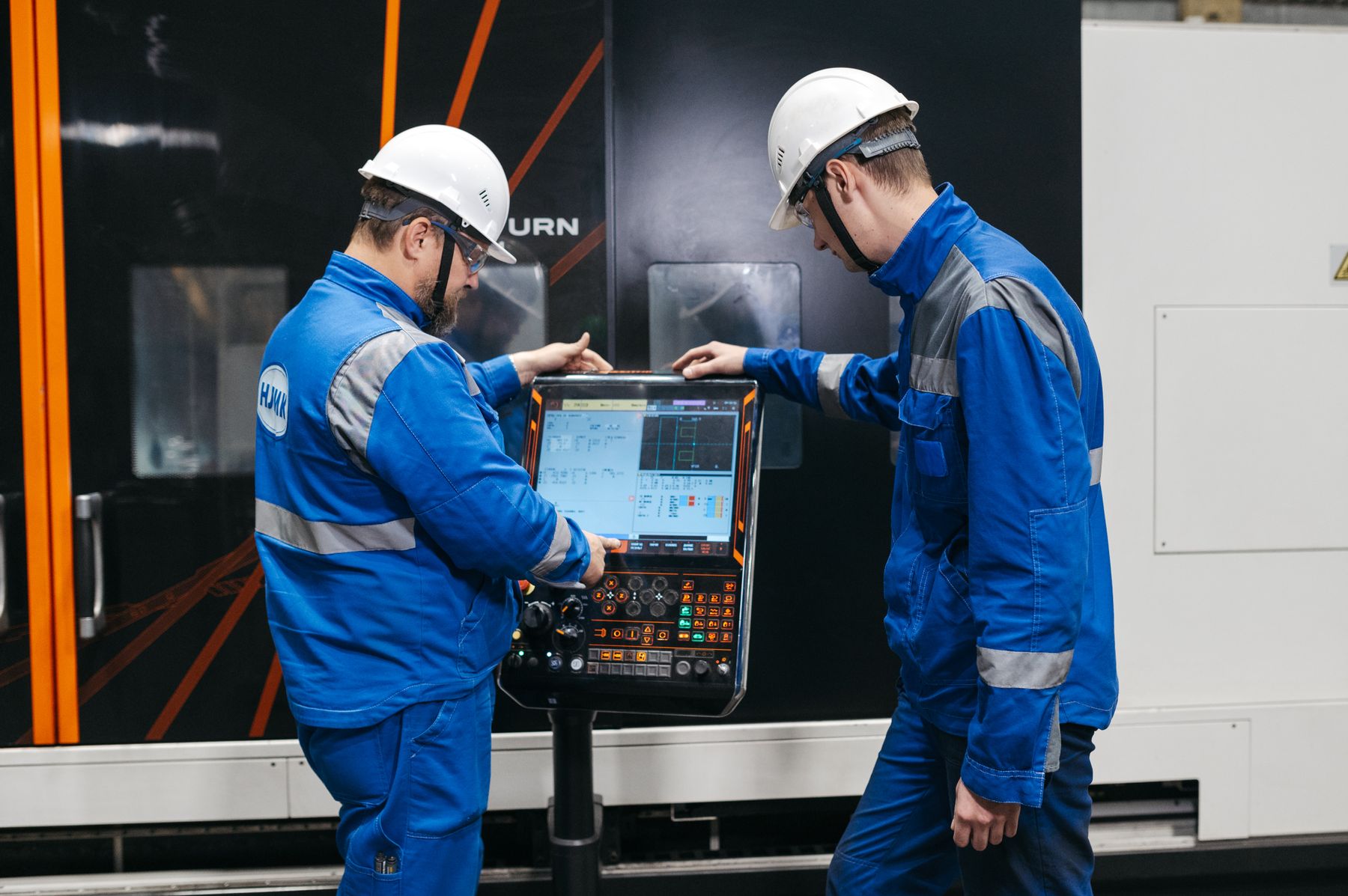 Two engineers reviewing a CNC machine control panel.